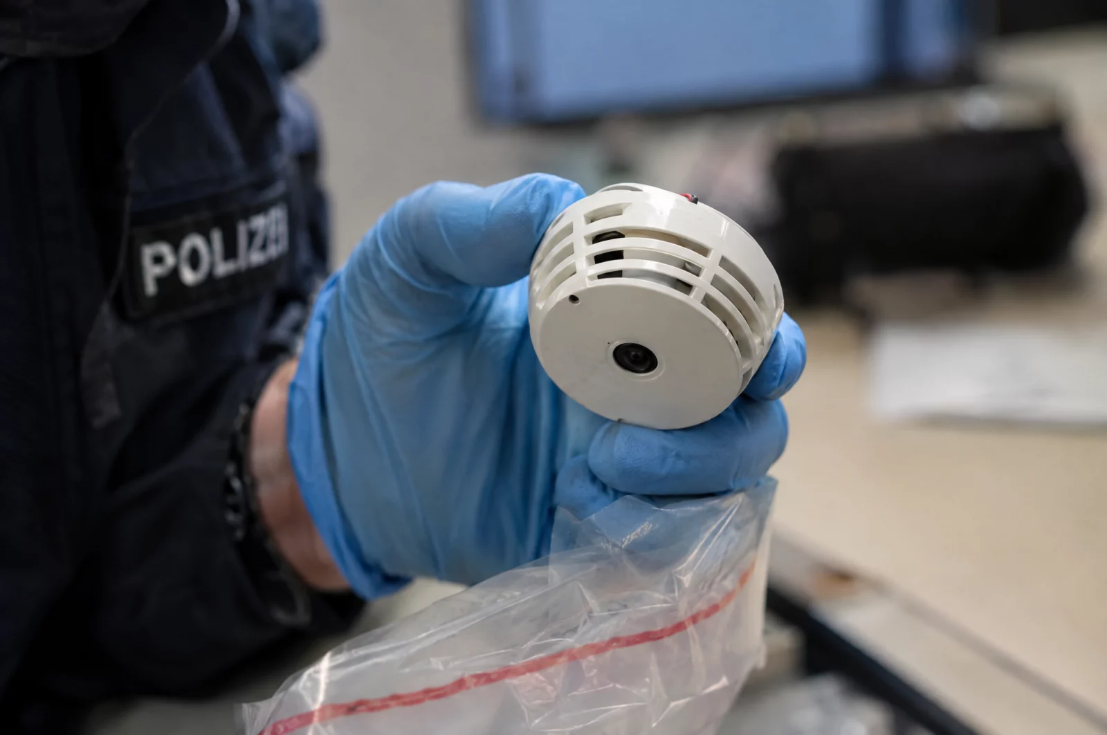 Verletzung des höchstpersönlichen Lebensbereiches durch Bildaufnahmen - § 201a StGB Eine im Rauchmelder versteckte Minikamera wird von einer Ermittlerin mit Handschuhen in eine Beweismitteltasche gelegt.