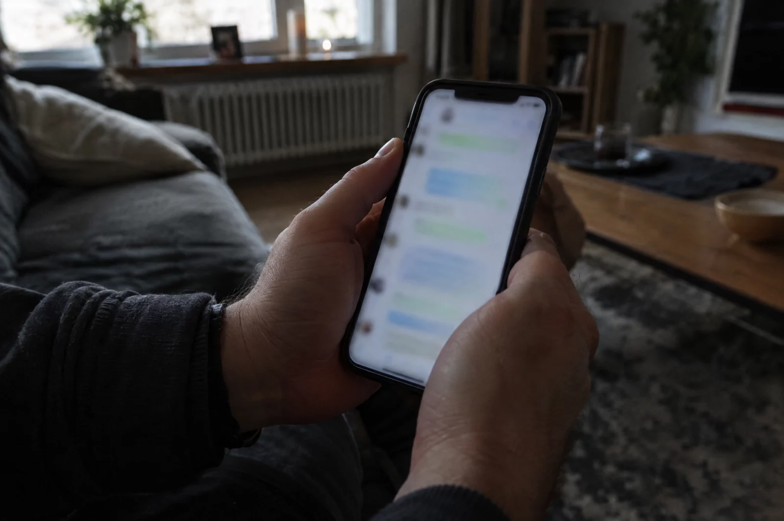 Hände halten ein Smartphone mit unscharfem Gruppenchat, Sinnbild für weitergeleitete Sticker und Bilder in Messenger-Gruppen.