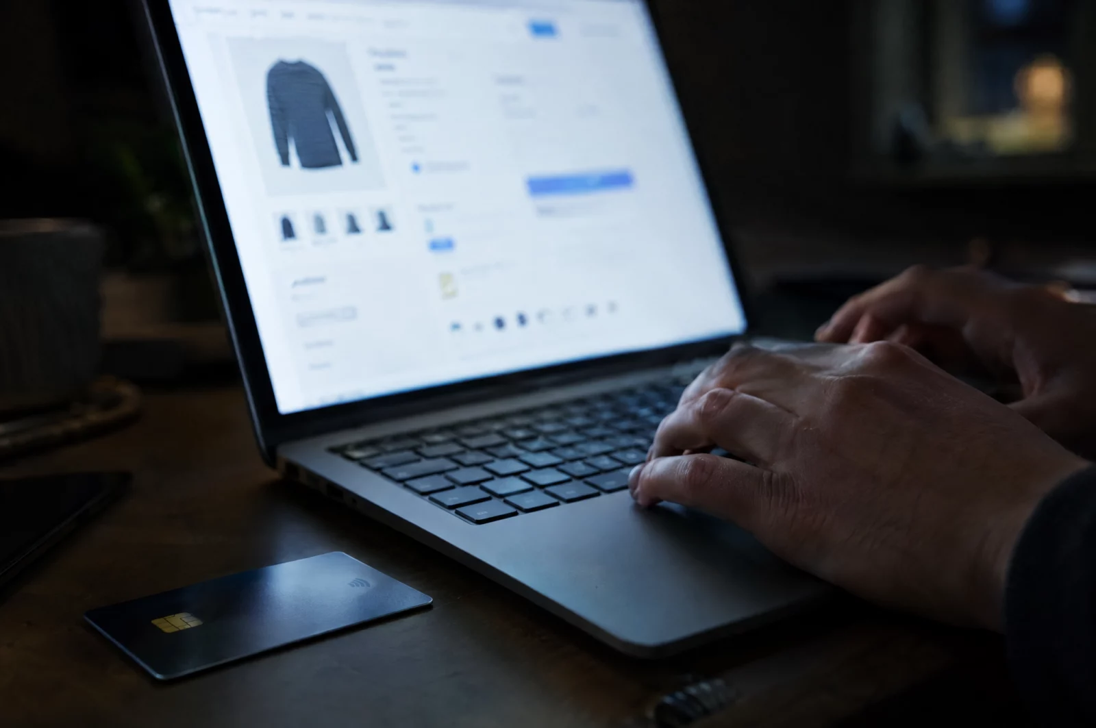 Finger tippen am Laptop im Bestellvorgang eines Onlineshops, daneben eine Kreditkarte, Szenario eines Computerbetrugs.
