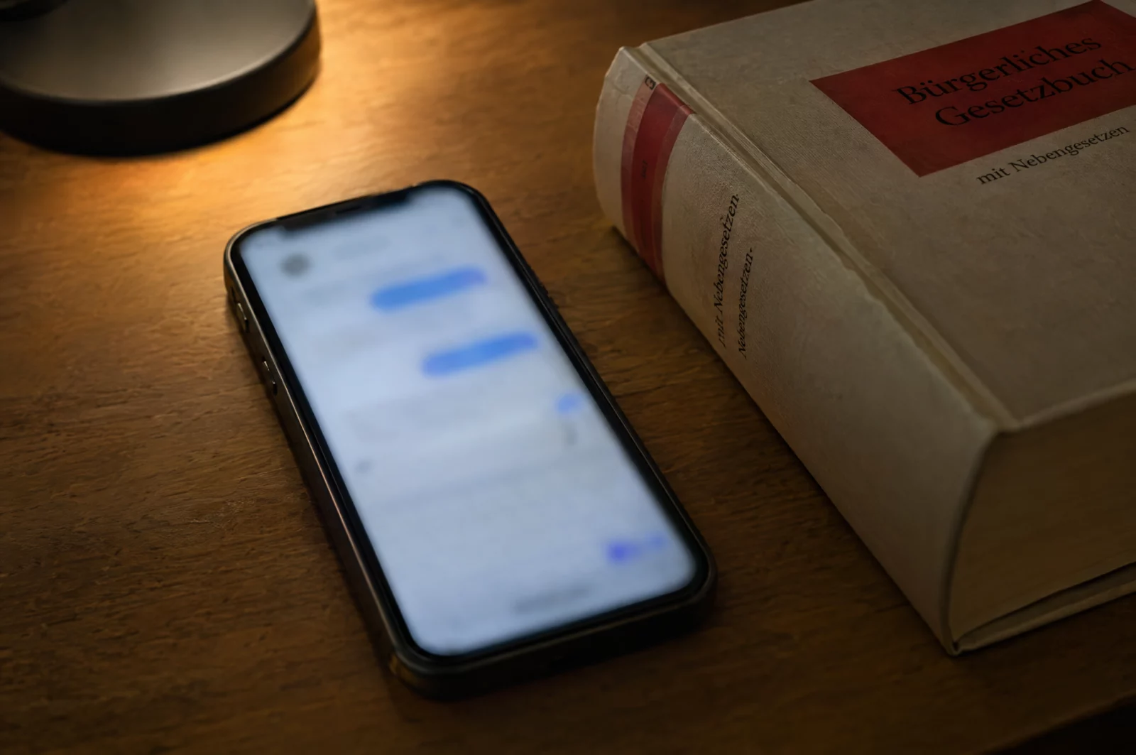 Smartphone mit unscharfem Chatverlauf liegt neben einem Gesetzbuch auf dem Schreibtisch, Sinnbild für den Vorwurf des Cybergroomings.