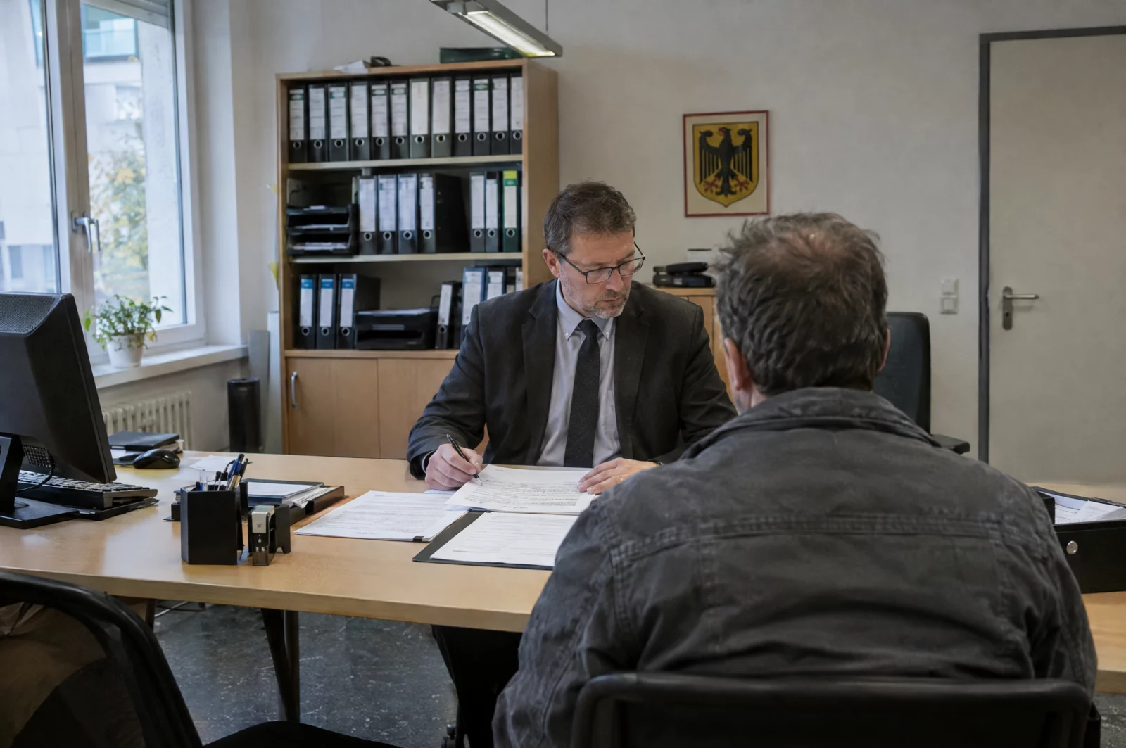 Mann sitzt bei der Vermögensauskunft einem Sachbearbeiter gegenüber – häufiger Anlass für eine falsche Versicherung an Eides Statt.