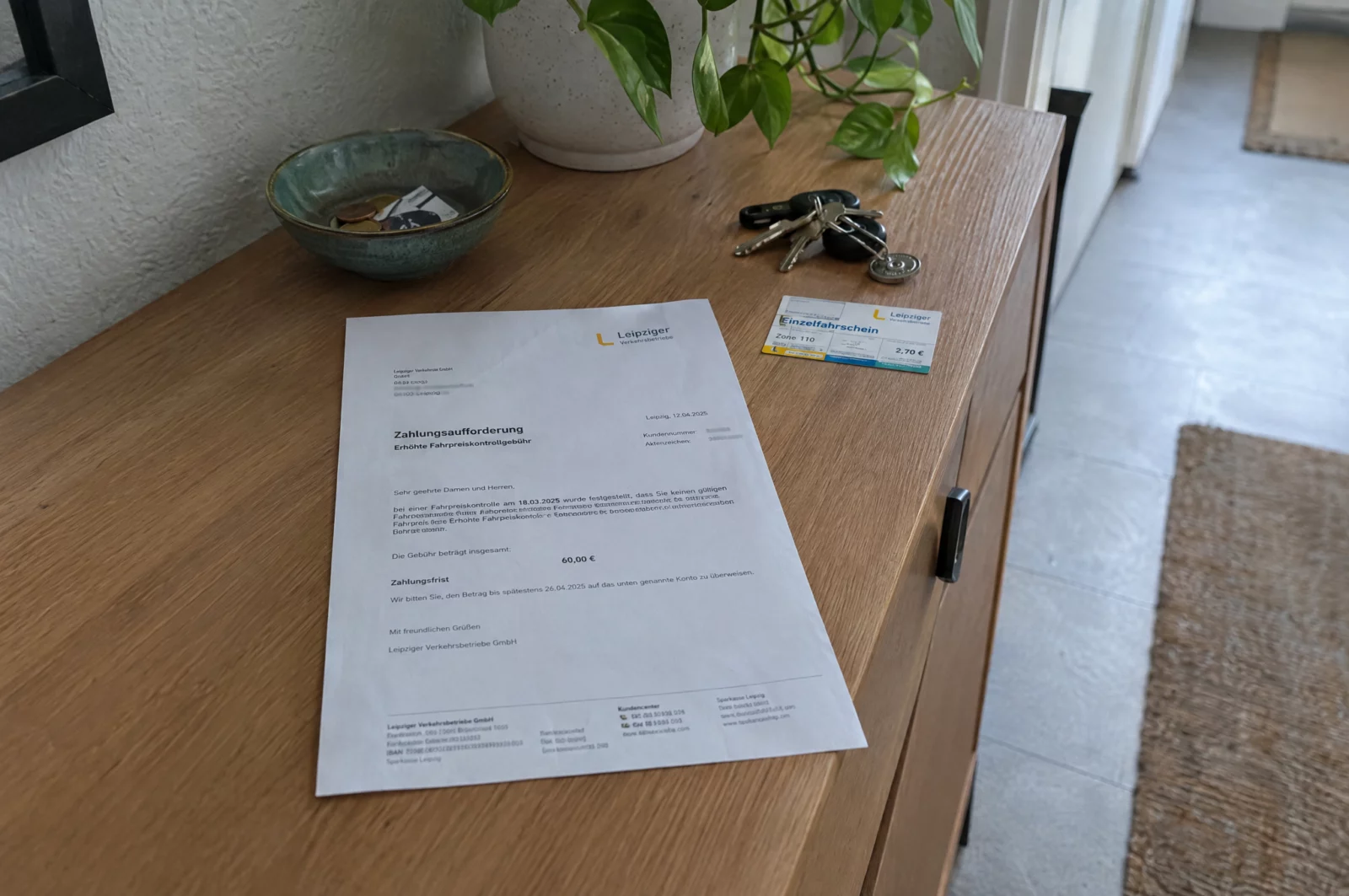 Ein Schreiben der Verkehrsbetriebe zum erhöhten Beförderungsentgelt liegt mit Schlüsseln und Fahrschein auf einer Kommode.