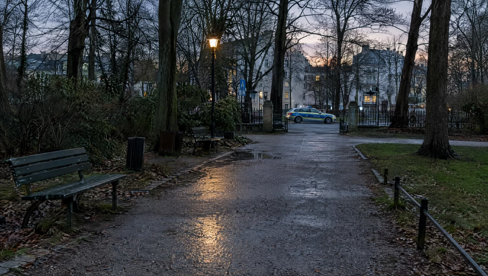 Ein leerer Parkweg in der Dämmerung, am Parkeingang steht ein Streifenwagen – häufiger Ort von Vorwürfen exhibitionistischer Handlungen.
