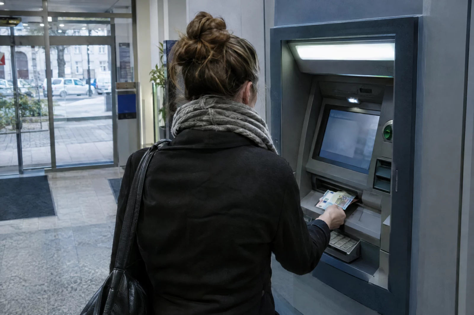 Person hebt am Geldautomaten einer Bankfiliale Euro-Scheine ab, wie es Finanzagenten bei der Weiterleitung von Geld tun.