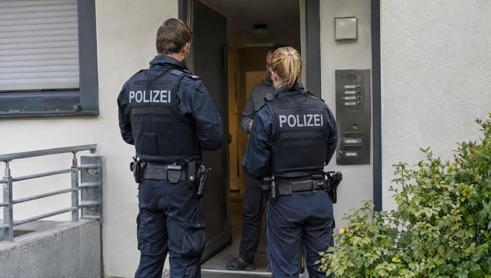 Zwei Polizeibeamte stehen an der Haustür eines Wohnhauses und sprechen mit einem Bewohner, typische Situation einer Gefährderansprache.