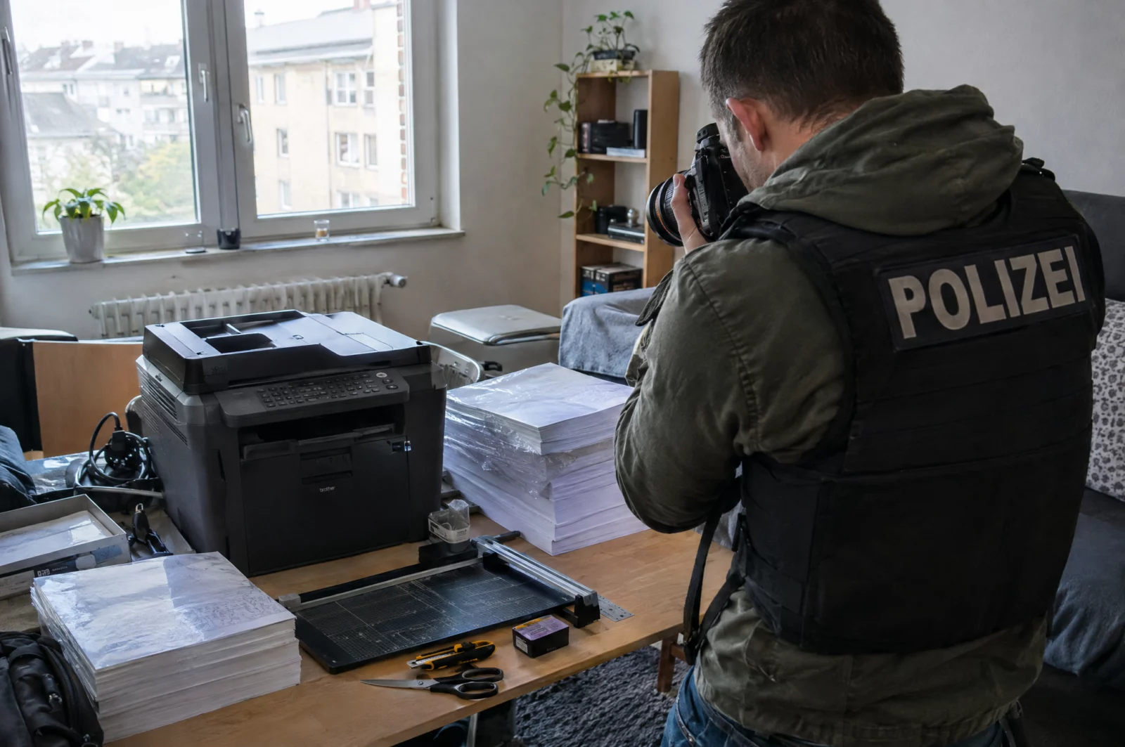 Bei einer Durchsuchung wegen Geldfälschung dokumentiert ein Ermittler einen sichergestellten Farbdrucker und Papierstapel.