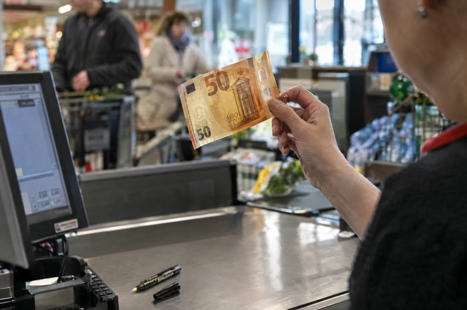An der Supermarktkasse hält eine Kassiererin einen 50-Euro-Schein gegen das Licht, um ihn auf Falschgeld zu prüfen.