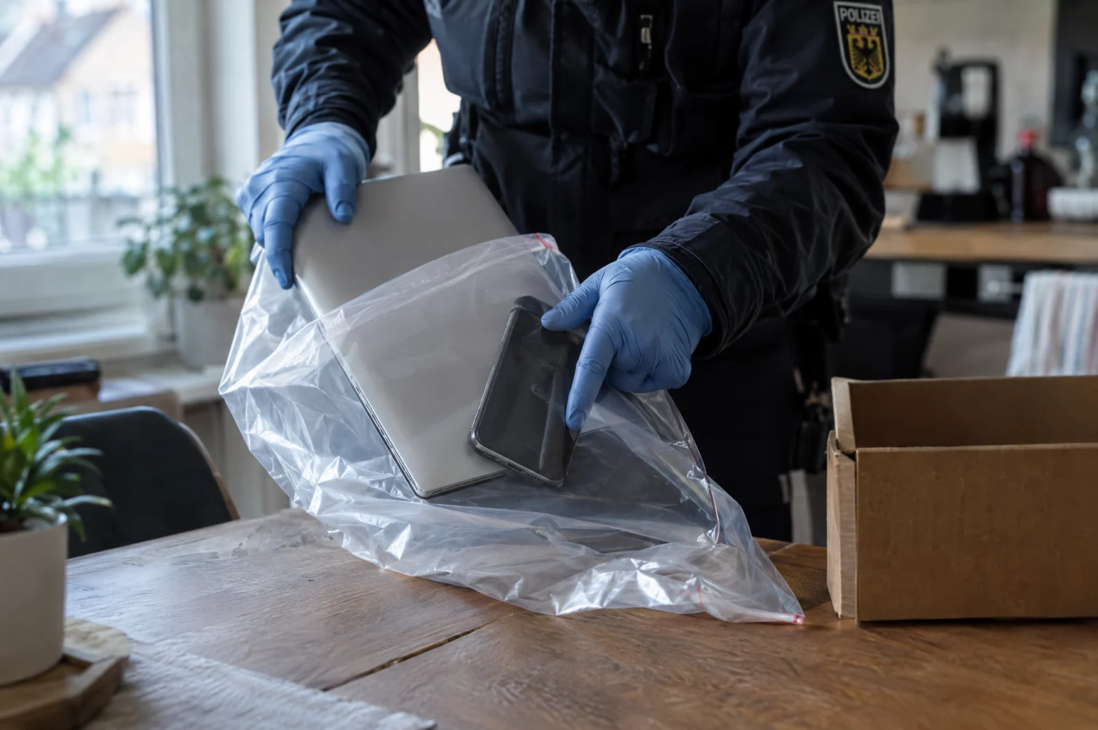 Polizeibeamter verpackt bei einer Durchsuchung Laptop und Smartphone als Beweismittel