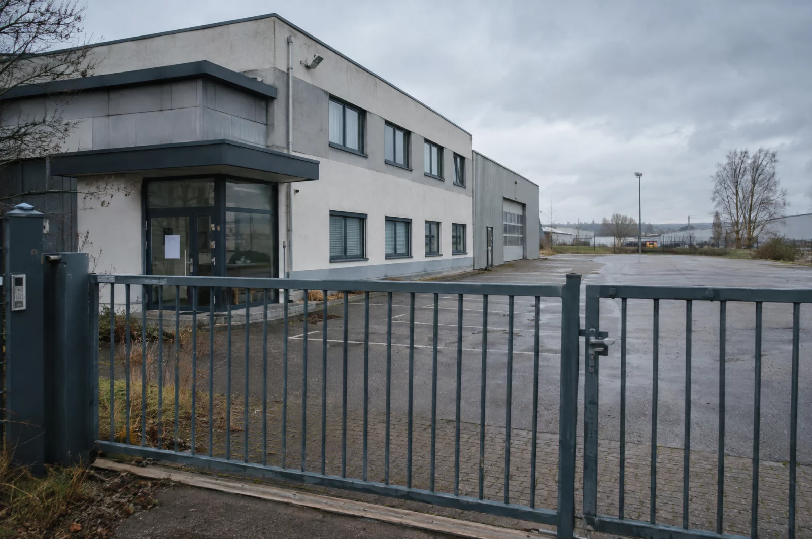 Verschlossenes Tor und leerer Parkplatz eines stillgelegten Betriebs im Gewerbegebiet nach Insolvenz des Unternehmens.
