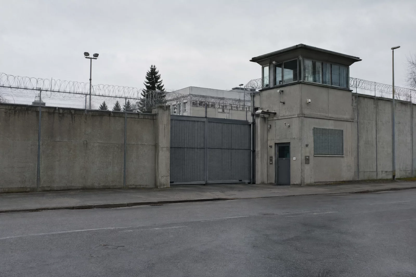 Hohe Betonmauer mit Stacheldraht und Pforte einer Justizvollzugsanstalt – die Kronzeugenregelung kann die Haftstrafe mildern.