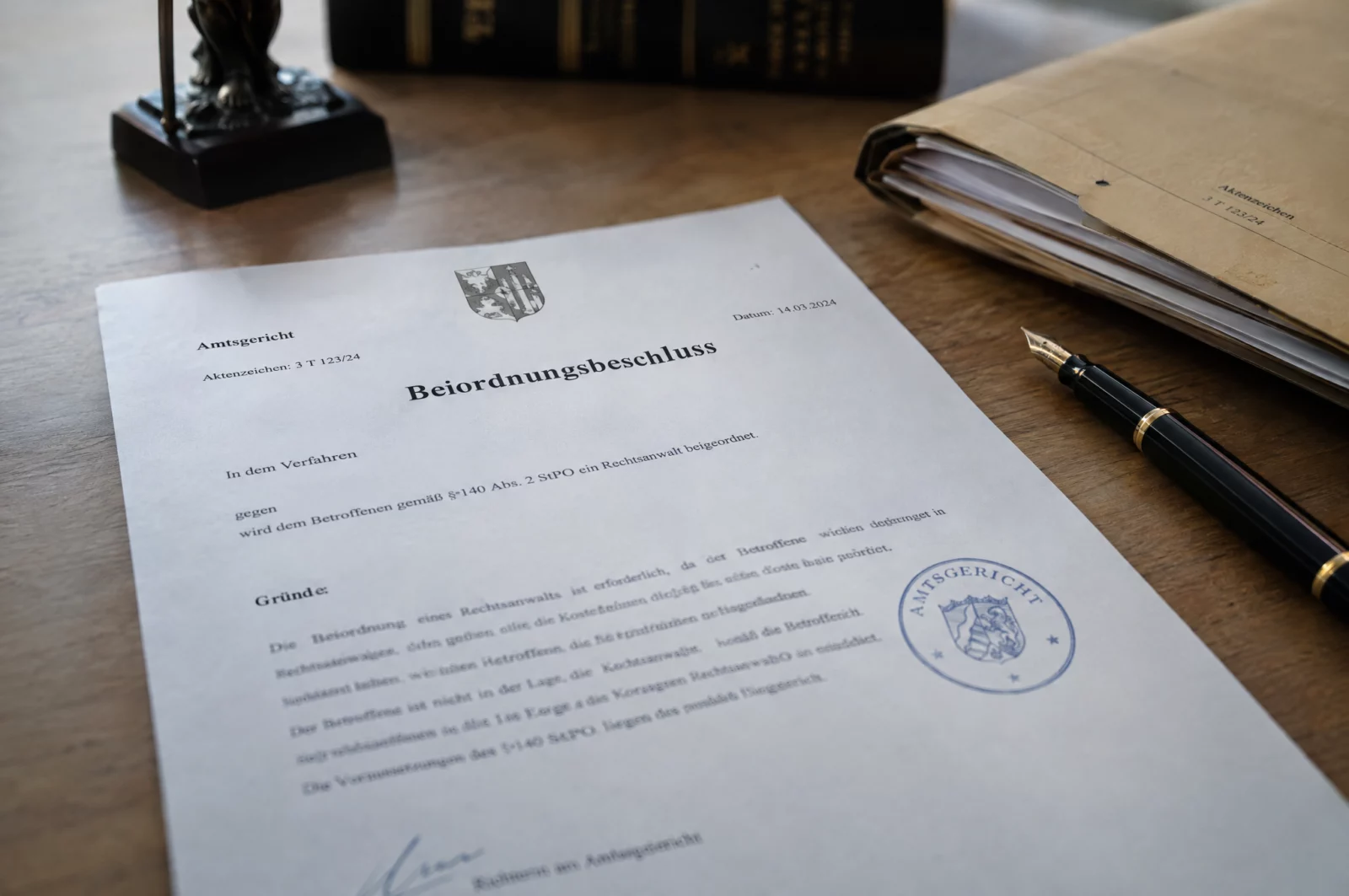 Ein gerichtlicher Beschluss mit Dienstsiegel liegt neben Füller und Akte, mit ihm wird ein Pflichtverteidiger beigeordnet.