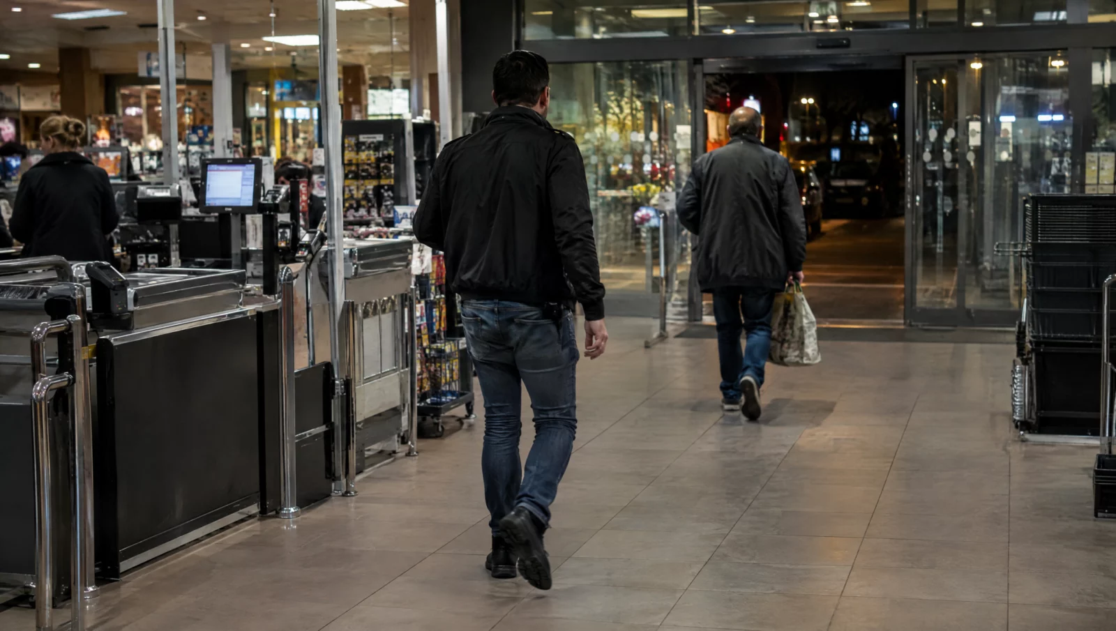 Ein Ladendetektiv geht im Kassenbereich eines Supermarkts auf einen Mann mit Tasche zu, Ausgangslage für räuberischen Diebstahl.