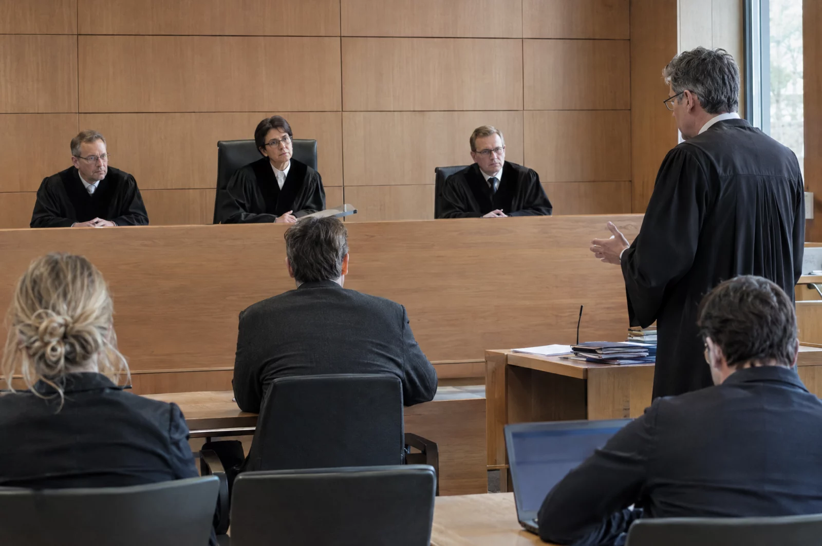 Drei Berufsrichter in Robe sitzen an der Richterbank, während der Verteidiger in der Berufungsverhandlung spricht.
