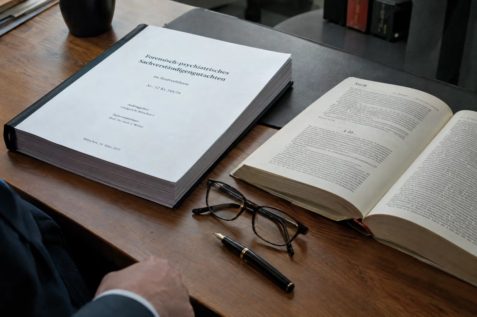 Gebundenes psychiatrisches Sachverständigengutachten neben einem aufgeschlagenen Strafgesetzbuch, Füller und Lesebrille.