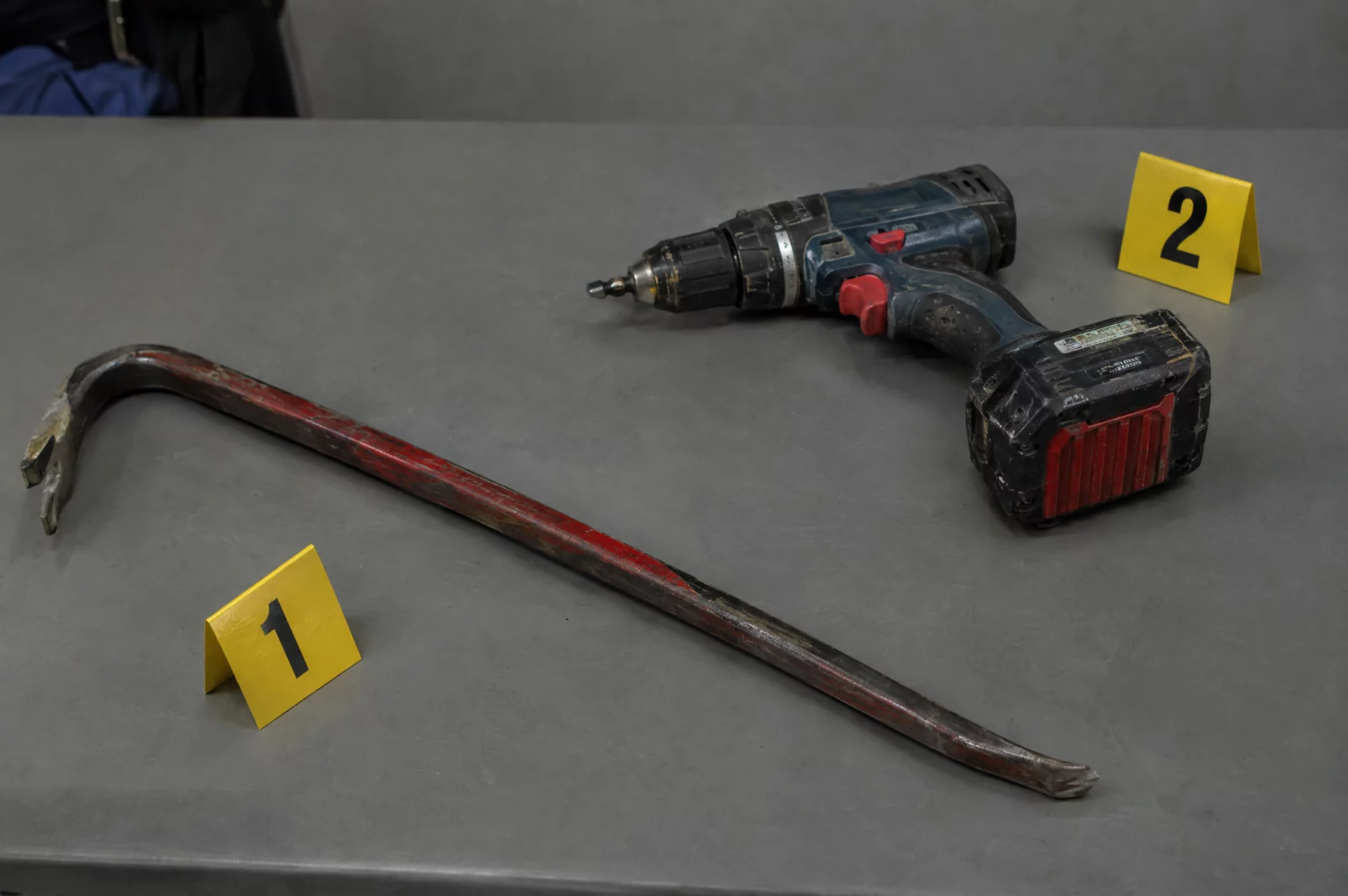 Besonders schwerer Diebstahl - § 243 StGB Brecheisen und Akkuschrauber liegen mit Nummernkarten auf einem Beweismitteltisch, sichergestellt bei Ermittlungen wegen Einbruchsdiebstahls.