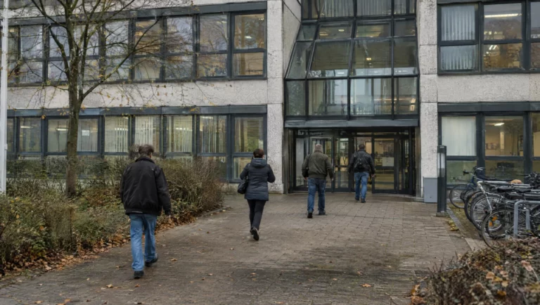 Menschen gehen auf den Glaseingang eines Jobcenter-Gebäudes zu, der Behörde, die bei Sozialbetrug Anzeige erstattet.