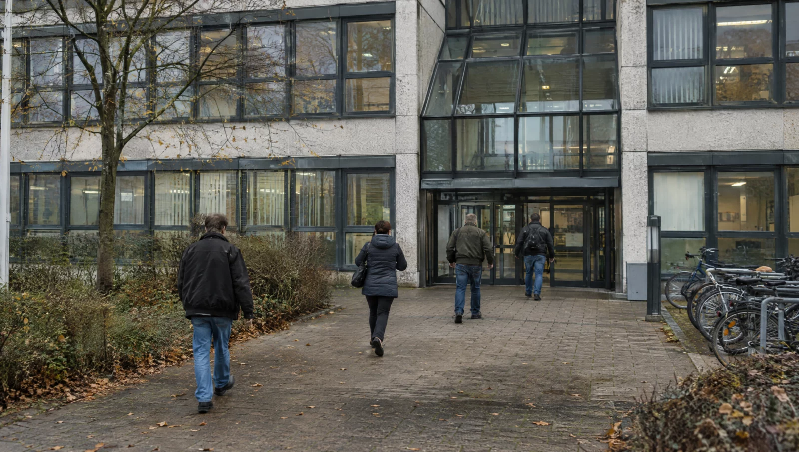 Menschen gehen auf den Glaseingang eines Jobcenter-Gebäudes zu, der Behörde, die bei Sozialbetrug Anzeige erstattet.