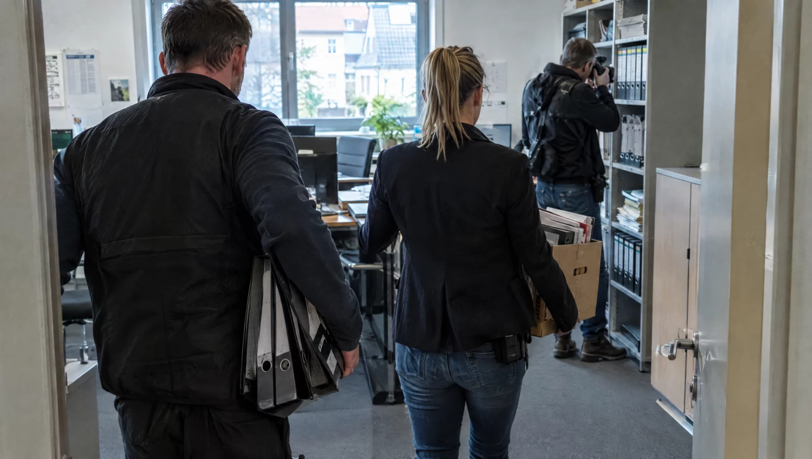 Steuerfahnder tragen Ordner und Kartons mit Geschäftsunterlagen aus einem Firmenbüro bei einer Durchsuchung wegen Steuerhinterziehung.