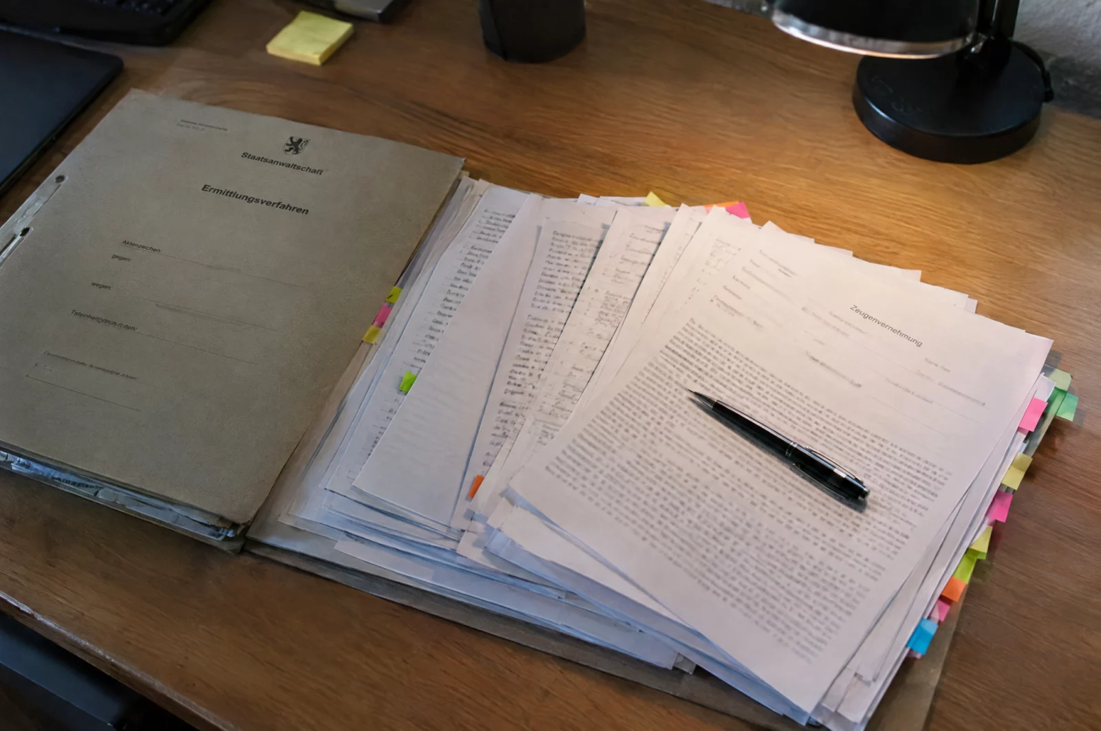 Aufgeschlagene Ermittlungsakte mit aufgefächerten Zeugenaussagen und Klebezetteln, Grundlage der Vorwürfe bei Straftaten aus Gruppen.