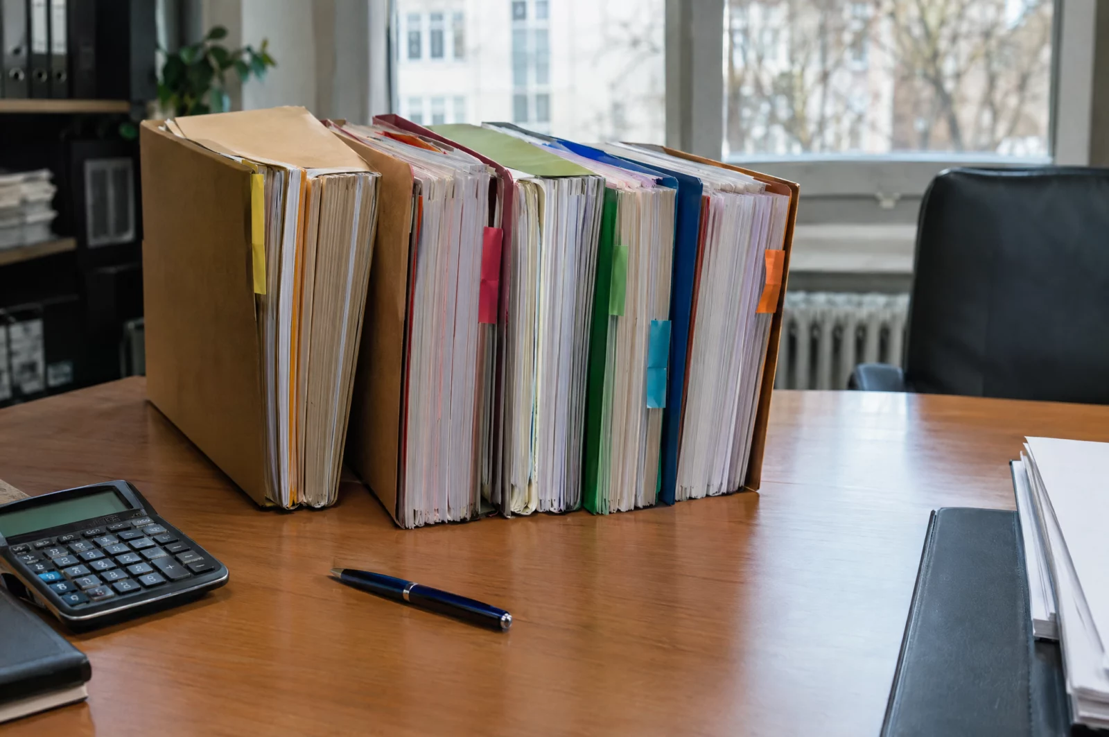 Mehrere Ermittlungsakten unterschiedlicher Dicke liegen nebeneinander mit Taschenrechner, Sinnbild für die Gesamtstrafenbildung bei mehreren Taten.