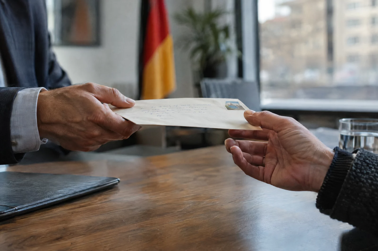 Eine Hand reicht über den Tisch einen handgeschriebenen Brief im Umschlag weiter, Geste der Wiedergutmachung beim Täter-Opfer-Ausgleich.