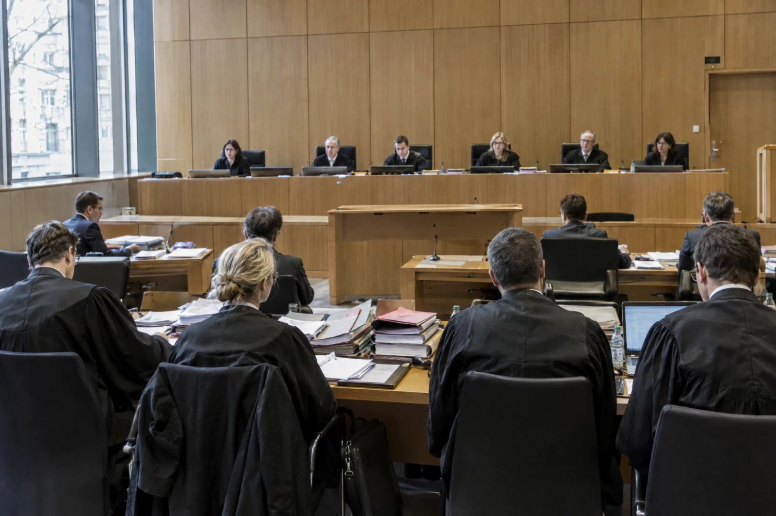 Großer Sitzungssaal einer Wirtschaftsstrafkammer mit Richterbank, mehreren Verteidigern in Robe und Aktenstapeln.