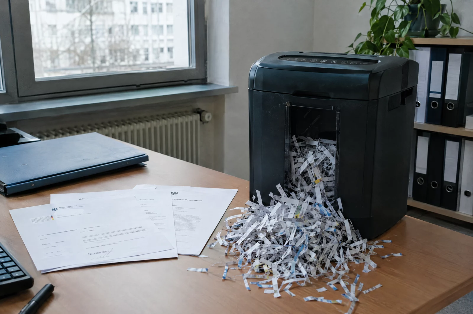 Ein Aktenvernichter mit halb geschredderten Papieren steht im Büro, ein typisches Bild für Urkundenunterdrückung.