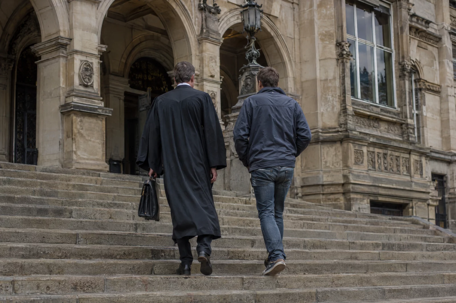 Verteidiger mit Aktentasche und Mandant gehen nach der Verhandlung die Sandsteintreppe eines Amtsgerichts hinunter.