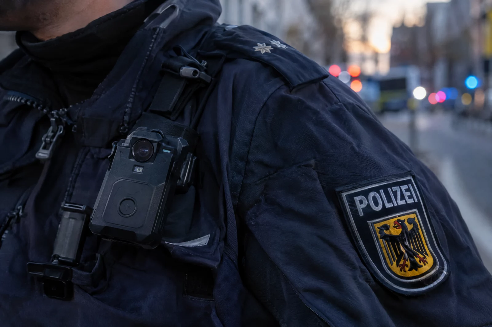 Nahaufnahme einer Bodycam an der dunkelblauen Uniform eines Polizisten, deren Aufnahmen bei Widerstandsvorwürfen zählen.