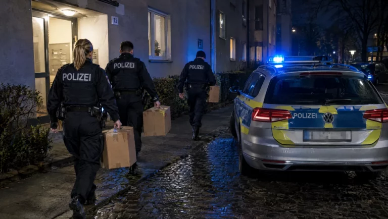 Polizeibeamte tragen nachts Kartons mit Beweismitteln aus einem Wohnhaus zum Streifenwagen, Ermittlungen wegen Zuhälterei.